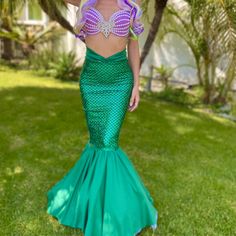 a woman in a green mermaid costume standing on the grass with her hands behind her head