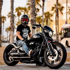 a man sitting on his motorcycle wearing a helmet and goggles with palm trees in the background