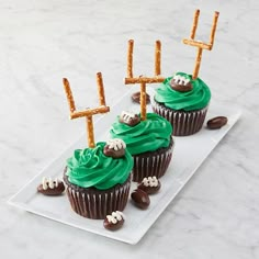 cupcakes decorated with green frosting and football decorations on a white platter