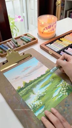 a person is painting with watercolors on a table next to a candle and some other items