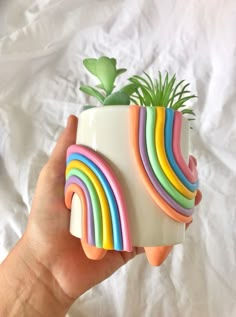 a hand holding a plant in a ceramic pot with rainbows painted on the sides