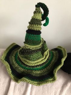 a crocheted hat with a green and black design on it sitting on top of a white blanket