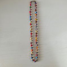 a multicolored beaded necklace hangs on a white wall with a metal hook