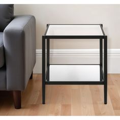 a black and white end table sitting on top of a hard wood floor next to a gray couch