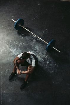 a man squatting on the ground with two barbells in front of him