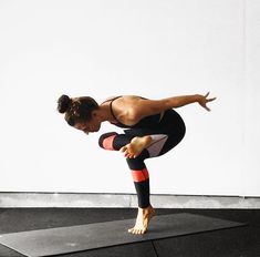 a woman in black and red doing a handstand on a yoga mat with her legs crossed