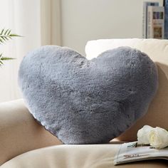 a gray heart shaped pillow sitting on top of a couch next to a white rose