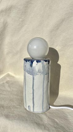 a white and blue ceramic table lamp on a white cloth covered surface with a shadow from the light bulb