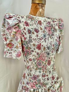 This is my 80s dream party dress. Polished cotton floral midi dress with the best princess sleeves. High neck with ruching through the bodice. Drop waist with a big attached bow. Full skirt. There is stretch through the torso, but the drop waist(hip area) is firm. Center back zip. Excellent condition. Washed and ready to wear. Marked 7/8.  MEASUREMENTS(taken flat, double when appropriate)  PTP 15-18 waist 12-16 dropped waist 15-18 length 49 This is the perfect unique gift for a loved one, or you 60s Drop Waist Dress, Spring Floral Print Puff Sleeve Dress With Fitted Bodice, Puff Sleeve Dress With Floral Print And Fitted Bodice, Floral Print Puff Sleeve Dress With Fitted Bodice, Fitted Puff Sleeve Dress With Ruffles For Garden Party, Fitted Puff Sleeve Dress With Smocked Back For Spring, Fitted Floral Print Puff Sleeve Dress For Garden Party, Spring Puff Sleeve Dress With Ruffles And Fitted Bodice, Garden Party Puff Sleeve Floral Dress With Fitted Bodice