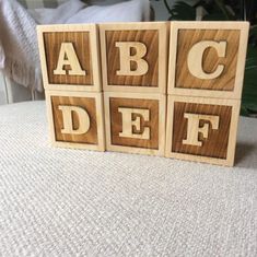 three wooden blocks with the letters abc, df and f on them sitting on a bed