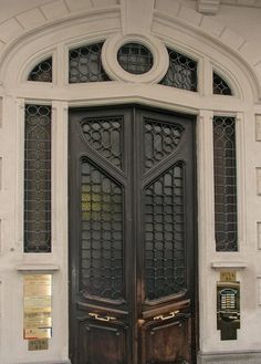 an ornate wooden door in front of a white building with arched glass panels and doors