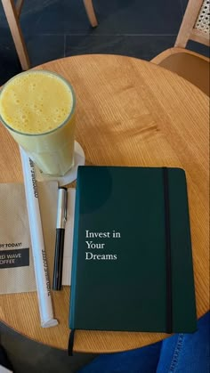 a notebook and pen sitting on top of a table next to a glass of orange juice