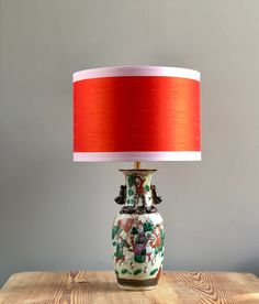 a lamp with a red shade on top of a wooden table next to a gray wall