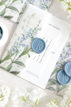 two blue wax seals sitting on top of a white envelope next to flowers and paper