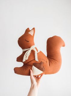 a hand holding a stuffed animal in the shape of a squirrel on a white background