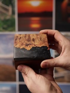 a hand holding a small wooden box in front of a wall with pictures on it