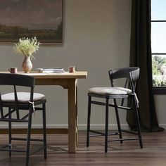 two chairs sitting at a table in front of a window with a painting on the wall