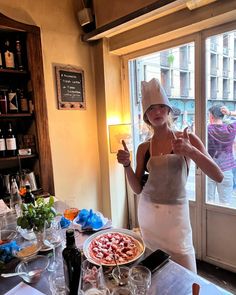 a woman standing in front of a table filled with food and drinks, giving the peace sign