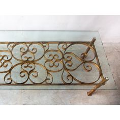 a glass and metal coffee table with scroll designs on it's sides, sitting on a marble floor