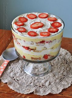 a trifle with strawberries on top sits on a doily next to a spoon