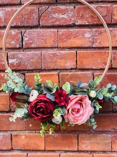 a hoop with flowers and greenery hanging on a brick wall