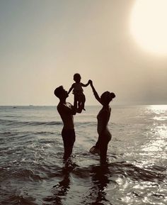 three people standing in the water with one holding a small child up to their chest