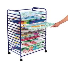 a person is holding a rack with many different colored papers on it and the bottom shelf has wheels