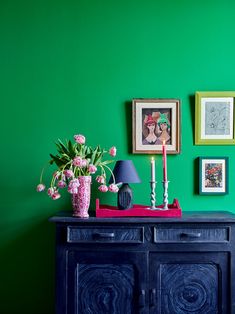 a room with green walls and pictures on the wall, flowers in a vase sitting on top of a dresser