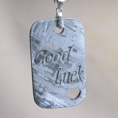 a metal dog tag with the words good luck on it hanging from a silver chain