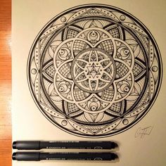 two pens are sitting on top of a paper with an intricate design in the middle