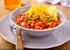 a white bowl filled with chili and tortilla chips on top of a wooden table