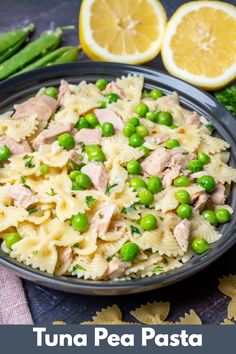 pasta with peas, ham and asparagus in a black bowl next to lemon wedges