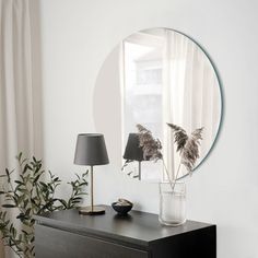 a black dresser with a mirror and lamp on it next to a plant in a vase