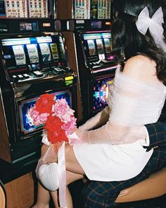 a woman sitting in front of a slot machine holding a bouquet of flowers and playing the game