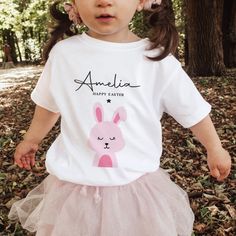 Easter bunny design kids t-shirt Presenting our personalised Happy Easter Kids T-Shirt, adorned with a cute bunny design tailored for boys and girls alike. This charming Children's T-shirt boasts a delightful bunny motif, perfect for adding an extra touch of Easter joy to your little one's wardrobe. With the option to personalise it with their name, this tee becomes a unique and heartwarming gift, especially fitting for a baby's First Easter celebration or a child's 1st Easter. Crafted with comfort and style in mind, this Bunny T-shirt serves as a wonderful Easter gift, embodying the spirit of the season and bringing a smile to your child's face with every wear. Cute White T-shirt With Bunny Design, Cute Crew Neck Top With Bunny Design, Cute T-shirt With Name Print For Gift, White Cotton T-shirt With Bunny Design, Cute Bunny Design Crew Neck T-shirt, Cute Bunny Design Short Sleeve T-shirt, Cute Bunny Design T-shirt, Cute Personalized Crew Neck T-shirt, Cute White Bunny Design T-shirt