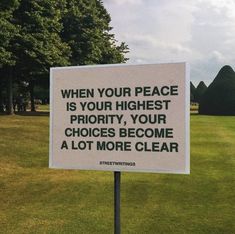 a sign that is in the grass with trees in the back ground and clouds in the sky