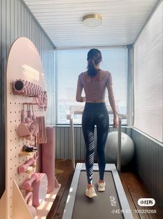 a woman standing on a treadmill in front of a window with her back to the camera