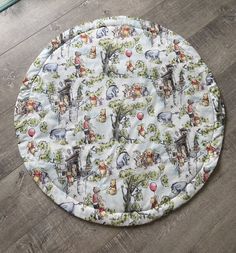 a round table cover with animals and trees on it, sitting on a wooden floor