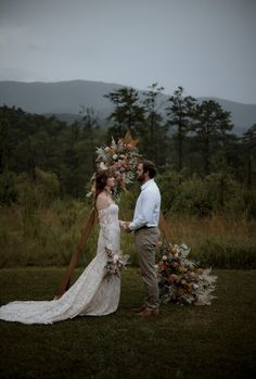 a bride and groom standing next to each other in front of a lush green forest