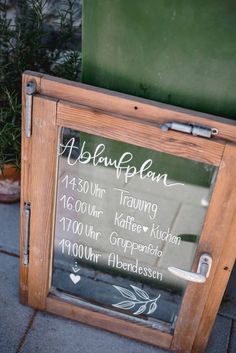 a wooden sign sitting on the side of a sidewalk next to potted plantes