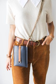 a woman wearing brown pants holding a blue and tan handbag in her right pocket