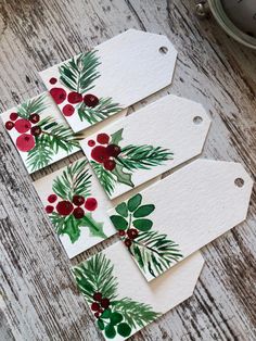 four tags with holly and berries on them sitting on a wooden table next to a clock