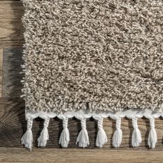 an area rug with tassels on top of it and wood flooring in the background