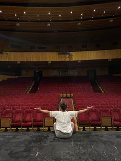 a man sitting on the floor in front of an empty auditorium with his arms outstretched