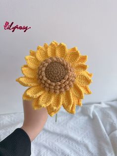 a crocheted sunflower being held up in the air by someone's hand