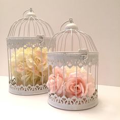 two white birdcages with pink roses in them sitting on a table next to each other