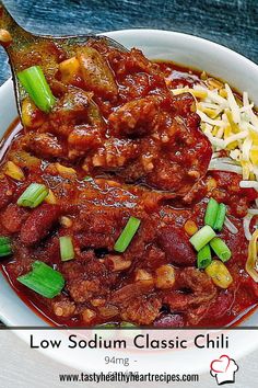 a close up of a bowl of food with chili and cheese on the side next to a spoon