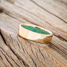 a gold ring sitting on top of a wooden table next to a green stone in the center