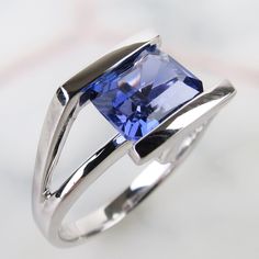 "A magnificent faceted 2 1/2 carat Tanzanite tops this contemporary Modernist 14k white gold ring. The 8.1mm x 6.5mm x 5mm purplish blue gemstone is tension-set tightly between thick solid bands of white gold. The ring was finished with a sleek shiny linear design which showcases different angles of the stone. The sturdy round band was made to last. The inside of the ring is hallmarked \"14k\" (white gold) and currently measures an approx. size 6.75. Please see photos and detailed measurements b Modern Sterling Silver Amethyst Ring For Formal Occasions, Modern Tanzanite Rings, Modern Tanzanite Jewelry For Promise Ring, Formal Faceted Blue Sapphire Ring, Formal Blue Faceted Sapphire Ring, Faceted Silver Sapphire Ring For Formal Occasions, Modern Sapphire Ring With Emerald Cut Diamond, Modern Emerald Cut Amethyst Ring, Modern Sterling Silver Sapphire Ring For Formal Occasions