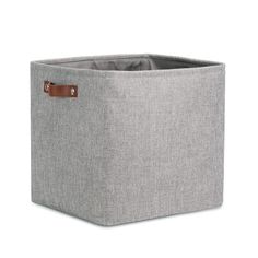 a grey fabric storage bin with leather handles on the front and side, it has a brown